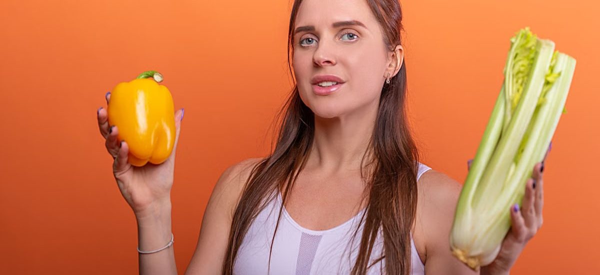 Woman holding yellow bell pepper and celery, showcasing healthy eating.