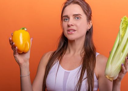 Woman holding yellow bell pepper and celery, showcasing healthy eating.