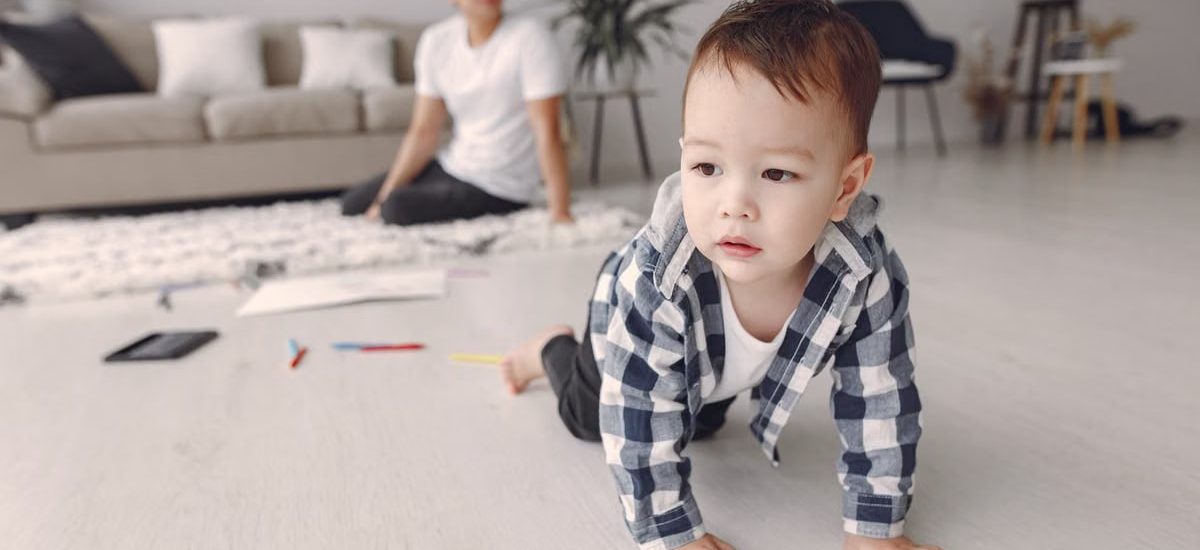 Cute baby boy crawling on the floor while dad watches in a cozy living room setting.