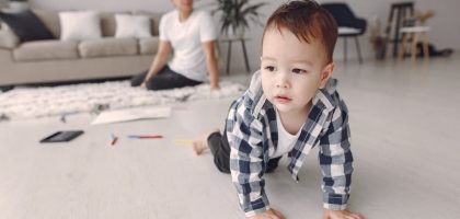 Cute baby boy crawling on the floor while dad watches in a cozy living room setting.