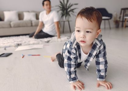 Cute baby boy crawling on the floor while dad watches in a cozy living room setting.